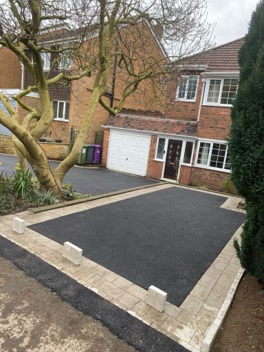 Tarmac Driveway A newly paved driveway with stone borders next to a brick house and trees.