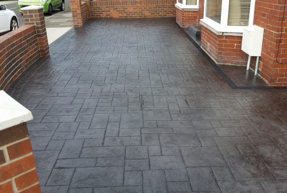 Imprinted Concrete Patterned dark grey paving stones in a driveway, bordered by brick walls.