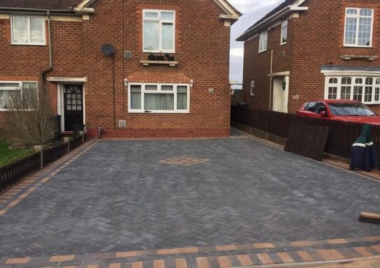 Block Paving Newly laid grey driveway with brick edges between two brick houses.